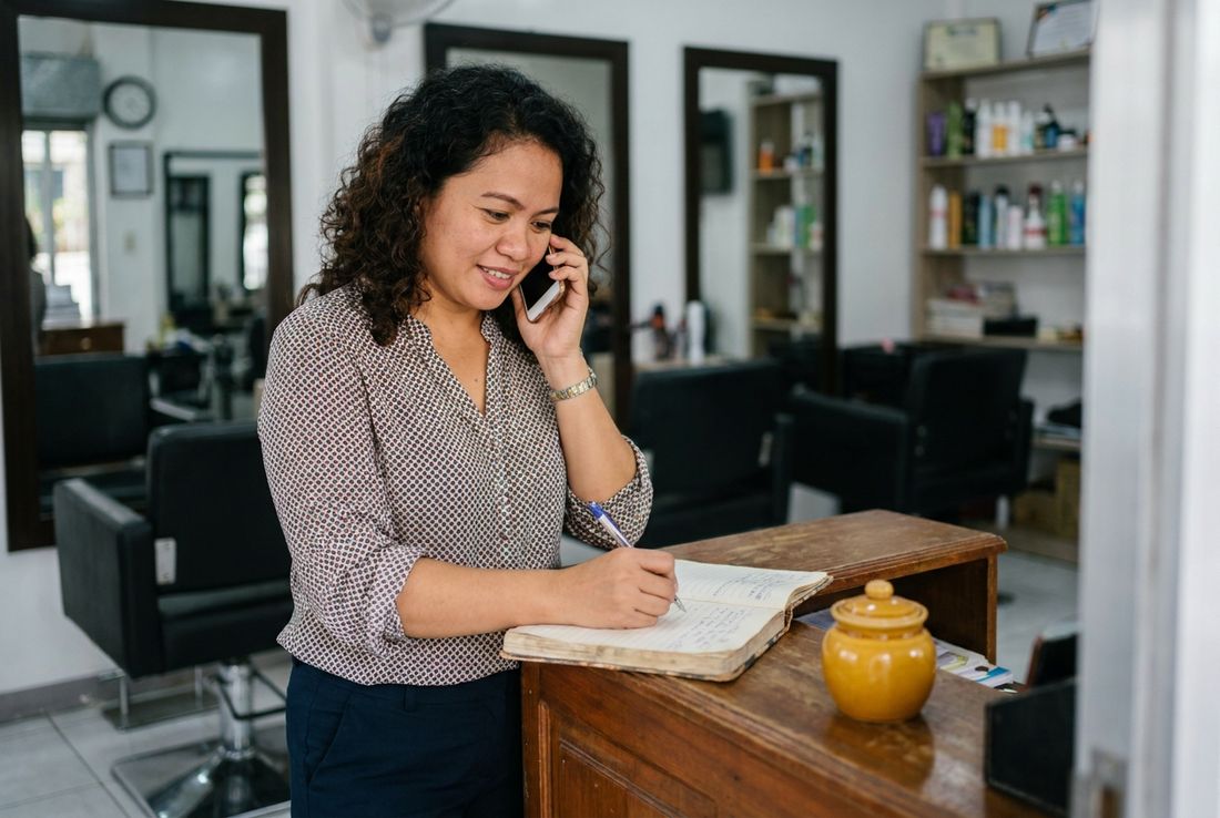 Salon owner taking a call at the reception counter and writing a note